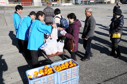 宿泊者にミカンなどをプレゼントし「いとうの日」をＰＲする小野市長ら＝伊東駅前観光協会大型バス駐車場