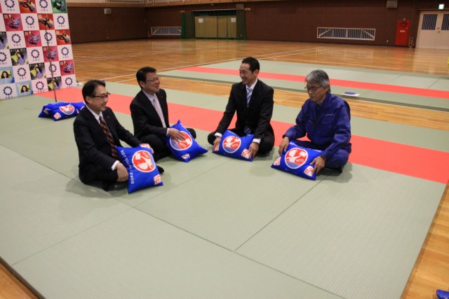 畳の上に座って言葉を交わす杉本常務（右から２人目）と小野市長（同３人目）ら＝伊東市民体育センター