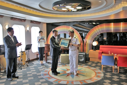 日野出ホテルマネジャー（中央右）から記念のレリーフを受け取る小野市長（同左）＝伊東港に錨泊する「ぱしふぃっくびいなす」船内