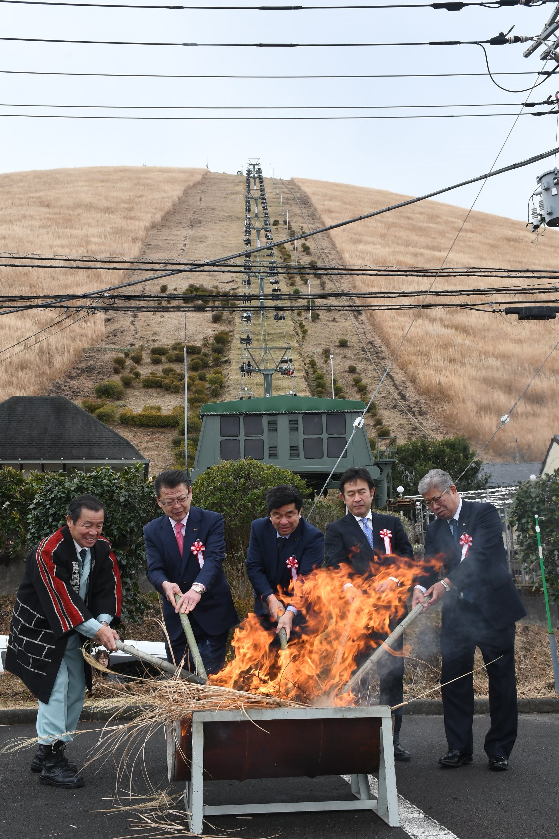 「採火式」でかやにたいまつで点火する高橋会長（左）と来賓ら＝伊東市の大室山リフト第２駐車場